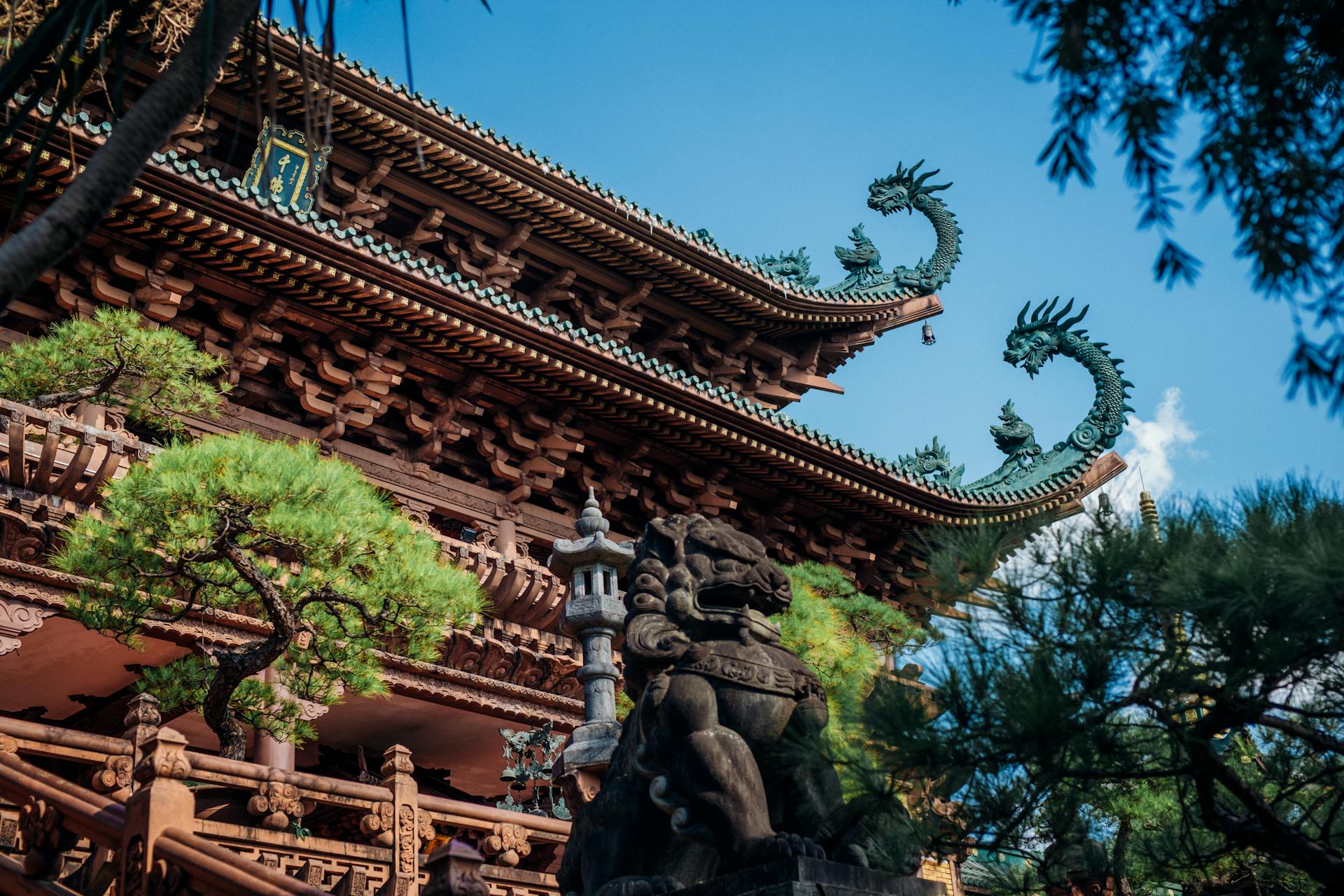 Intricate dragon sculptures adorn the eaves of an ancient pagoda, surrounded by lush greenery.