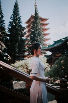 一位身着传统服装的亚洲妇女，侧身静立在宁静花园的佛塔旁