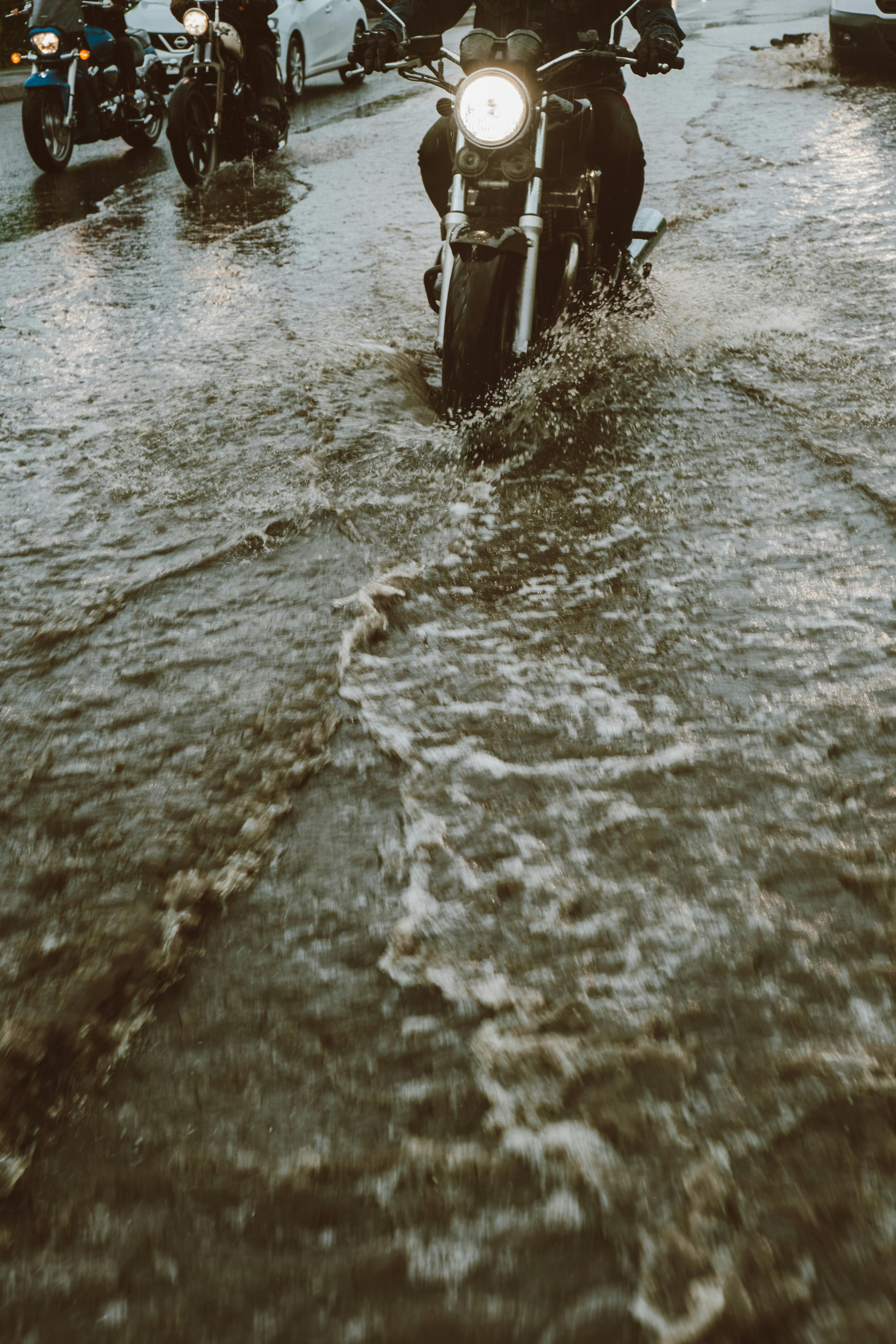 A motorcycle navigates a flooded street, headlights glowing, capturing urban resilience.