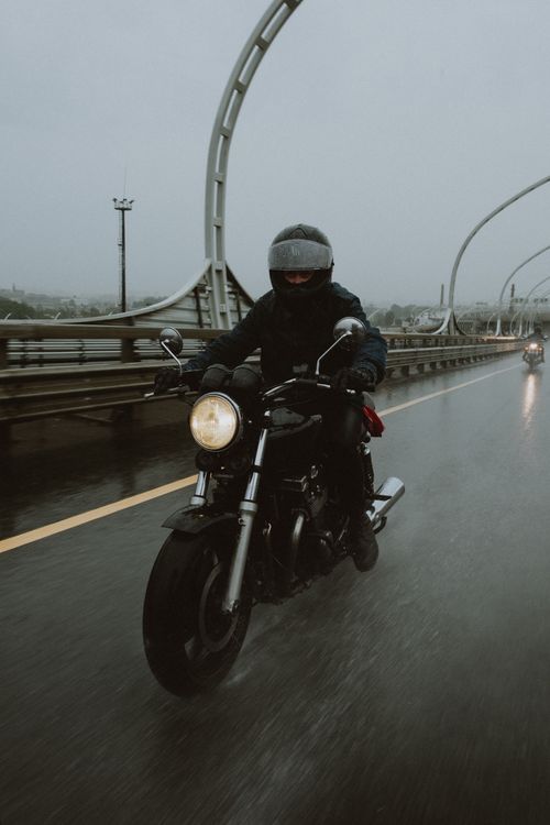 Free A lone rider on a motorcycle braves a rainy day on a modern highway bridge. Stock Photo