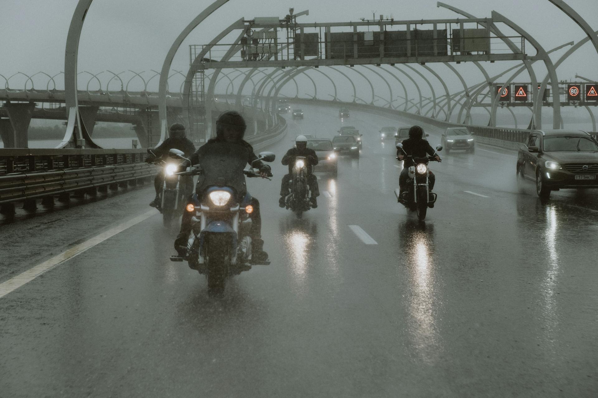 Group of motorcyclists riding through rain on a modern city highway with wet roads.