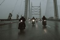 在多云的天气里，摩托车手骑过一座桥，营造出戏剧性的场景