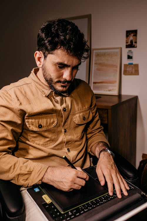 Free Ethnic man working on laptop and drawing on graphic tablet Stock Photo