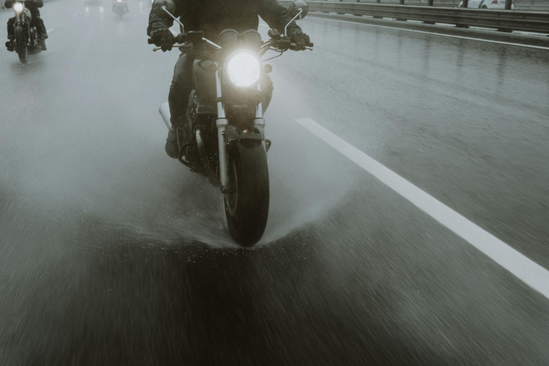 Motorcyclists navigate a wet highway at night, splashing water during their ride.