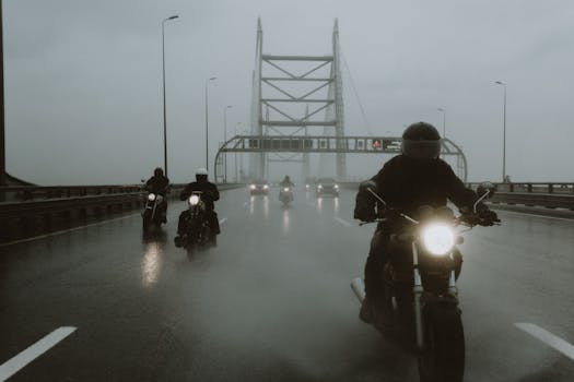 Group of motorcyclists riding on a wet bridge under a gloomy sky.