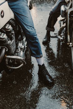 Bikers stand beside motorcycles on a wet pavement during rain.