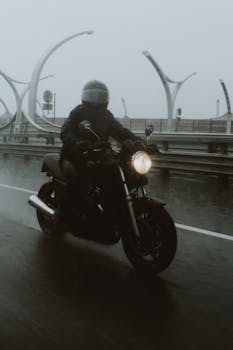 A motorcyclist rides through rain on a wet highway, highlighting transport resilience.