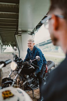 A man joyfully sitting on a motorcycle beneath a bridge, depicting adventure and freedom.