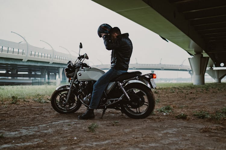 Man In Black Jacket Sitting On A Motorcycle Putting On His Helmet