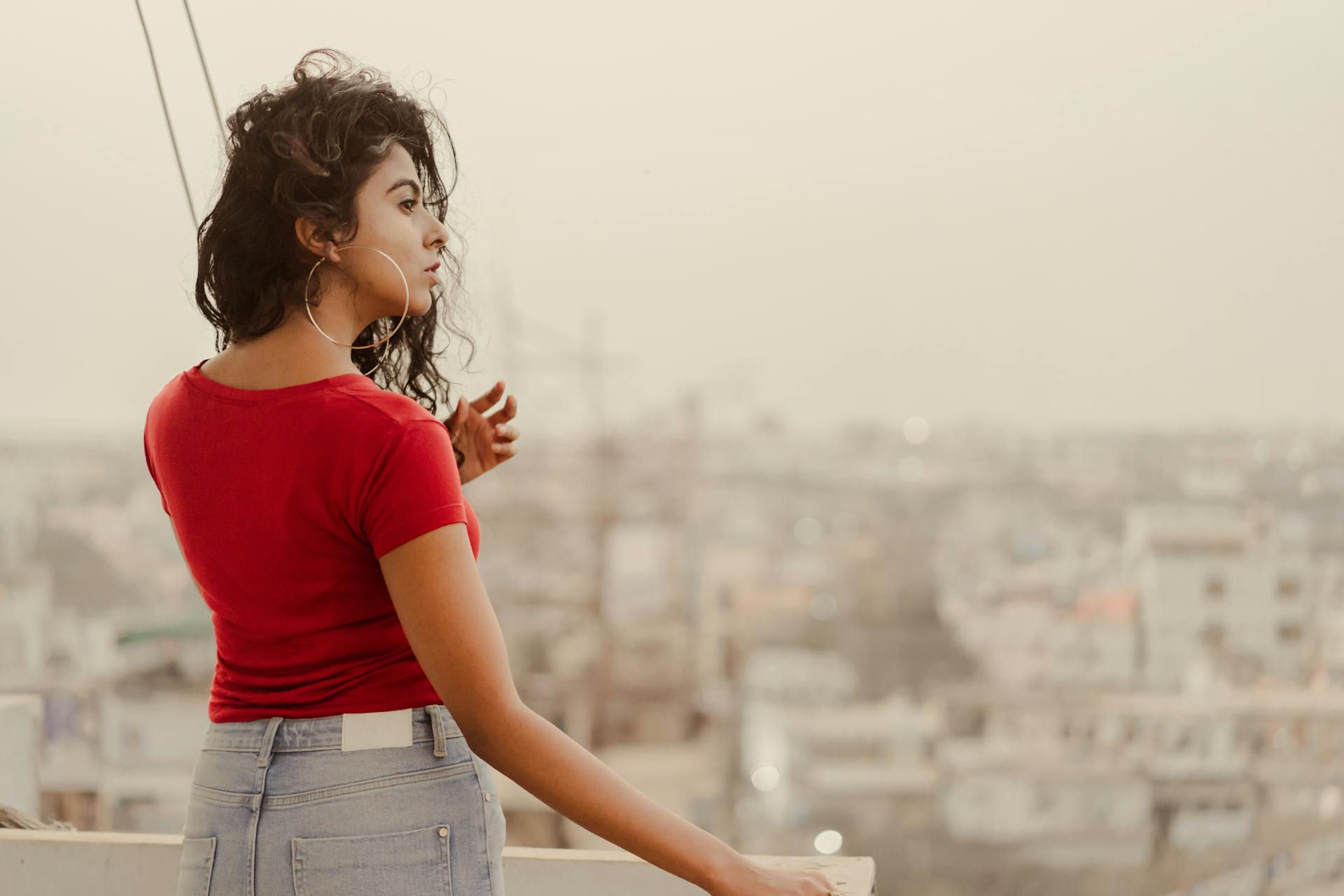 Woman in red top overlooking Hyderabad cityscape from rooftop at sunset.