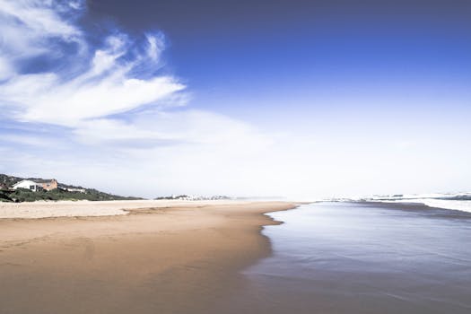 Tranquil sandy beach with blue skies in Wilderness, South Africa, offering a serene coastal view.