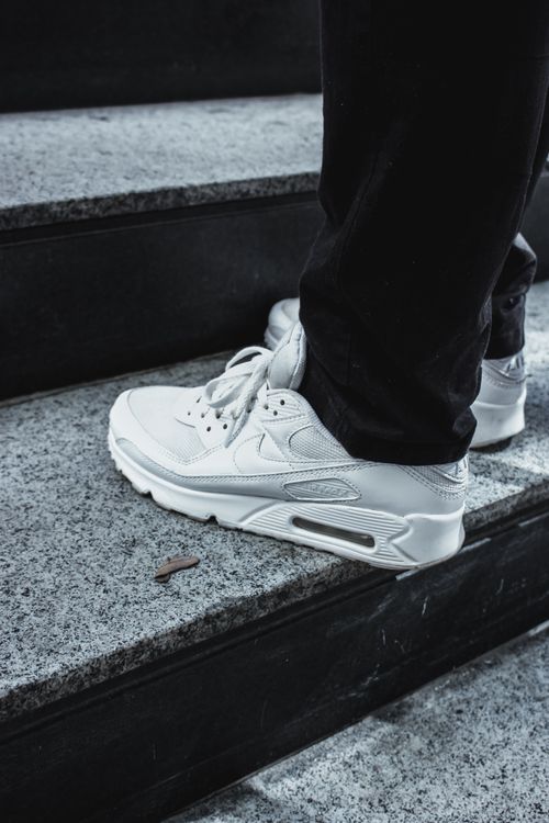 Free Close-up of classic white sneakers stepping on black granite stairs, showcasing modern street fashion. Stock Photo