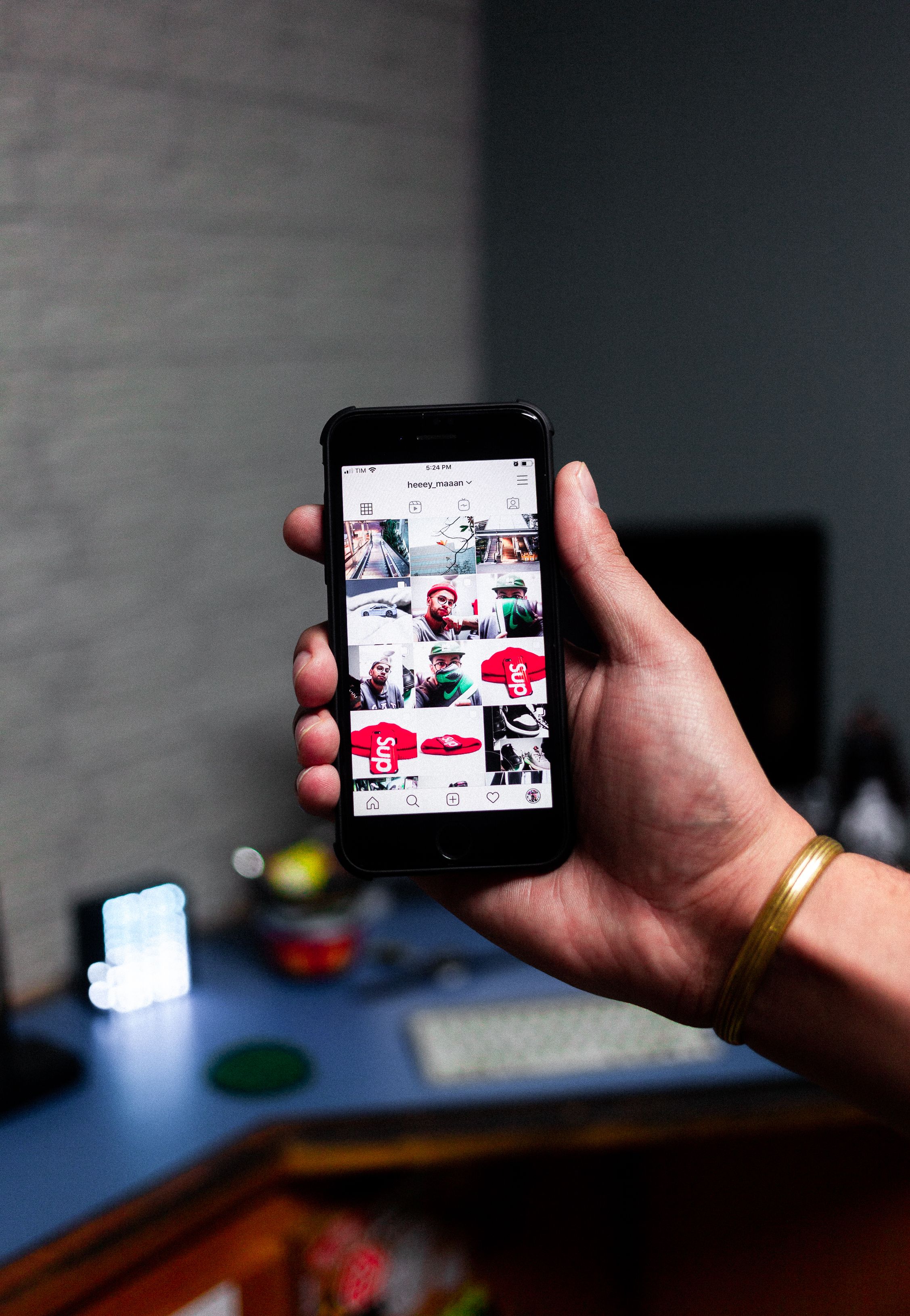 Person holding a smartphone displaying an Instagram feed indoors.