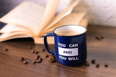 A blue enamel mug beside an open book on a wooden table