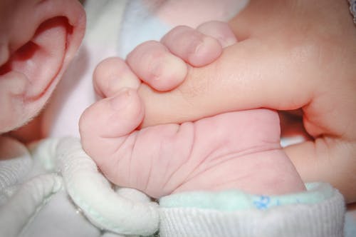 Touching moment of crop anonymous newborn infant with tiny hand lying on soft bed and gently grasping parents finger