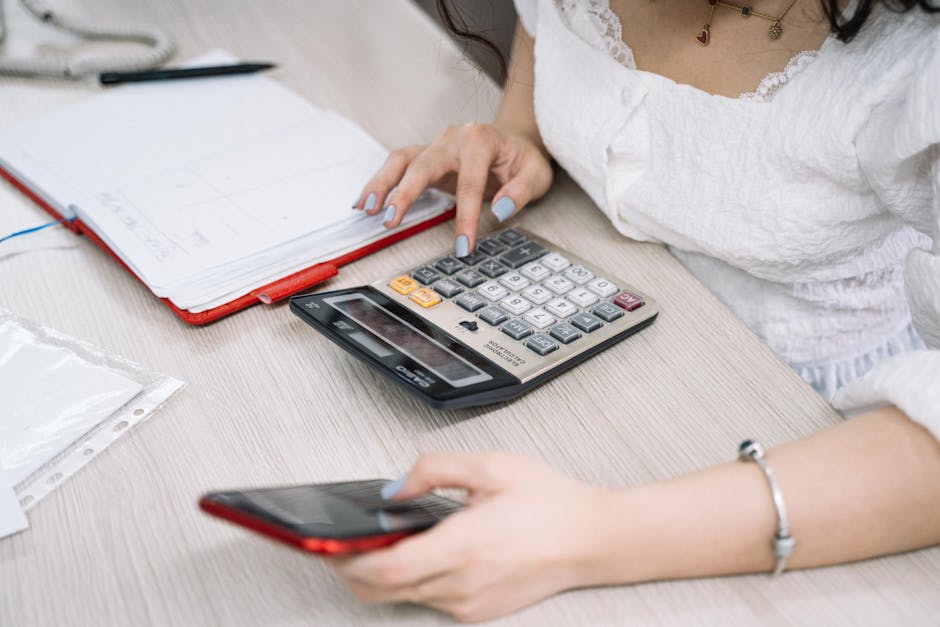 Close-up of a woman using a calculator and phone at her office desk.