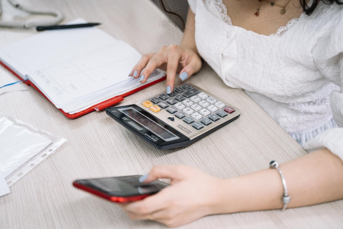 Free Woman Using a Black and Red Smartphone and Calculator Stock Photo