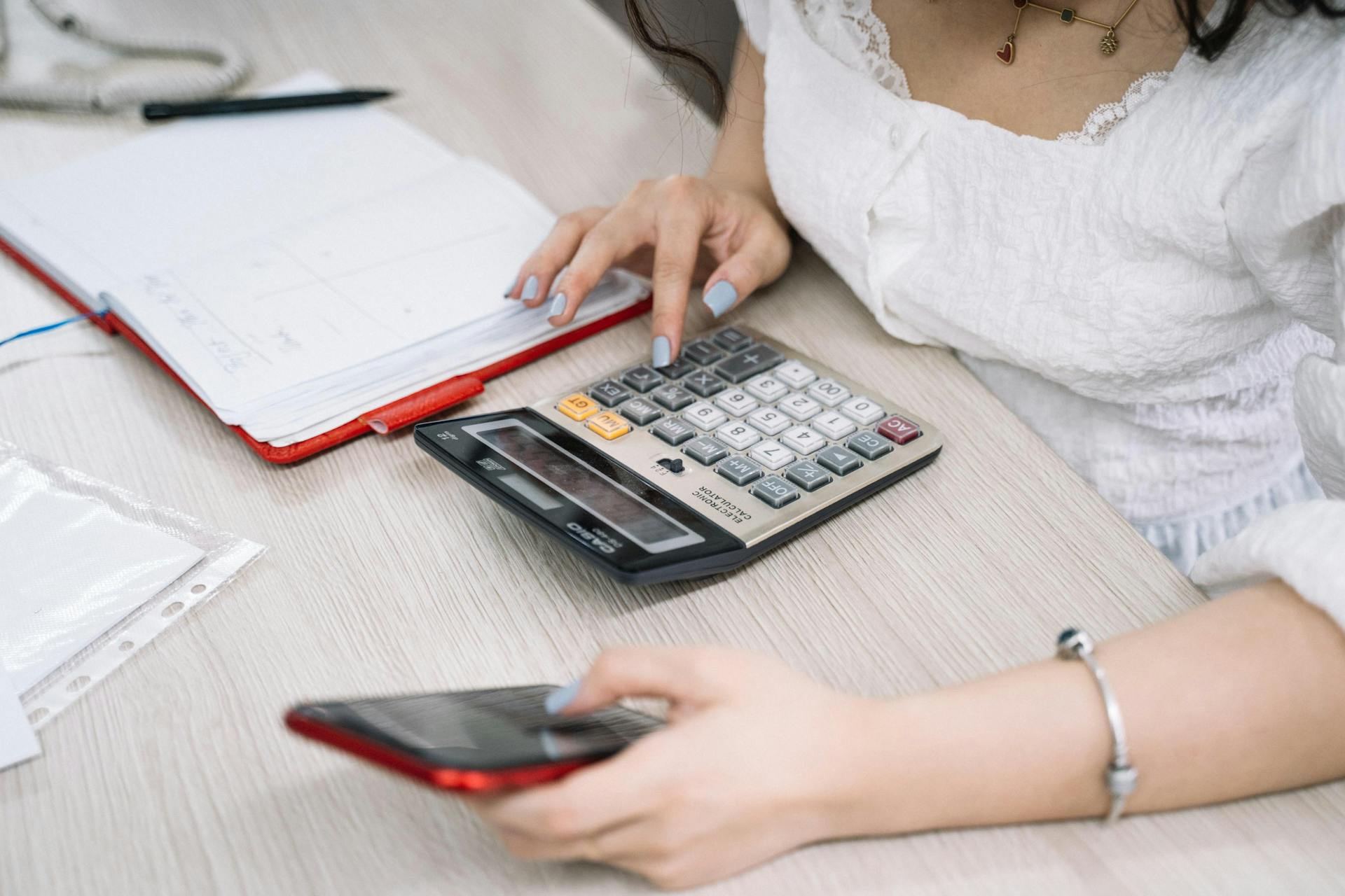 Close-up of a woman using a calculator and phone at her office desk.