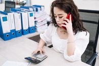 女商人用计算器和手机在办公桌上进行多任务处理