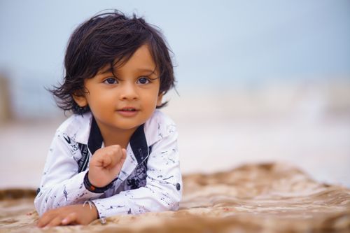 Free Cute child with black hair smiling and lying on a beach blanket outdoors. Captures innocence and joy. Stock Photo