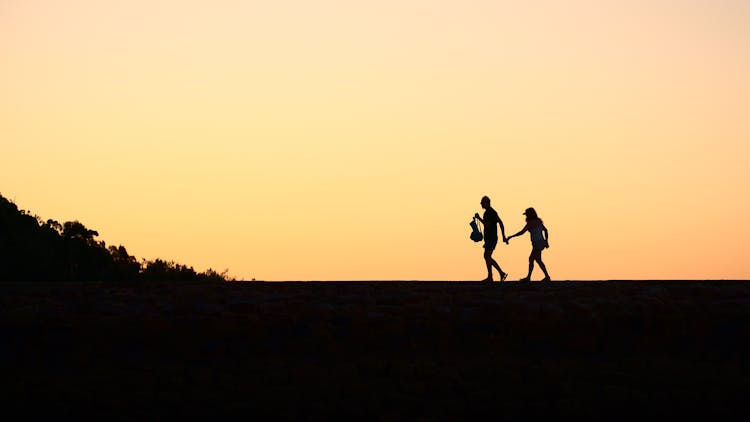 Silhouette Of People Walking While Holding Each Others Hands Under Golden Sky