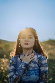 A young woman poses outdoors with backlighting highlighting her colorful hair accessories.