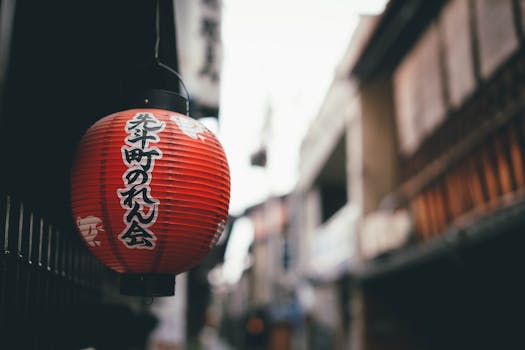 Red Japanese lantern with kanji script hanging on a traditional street, blurred background.