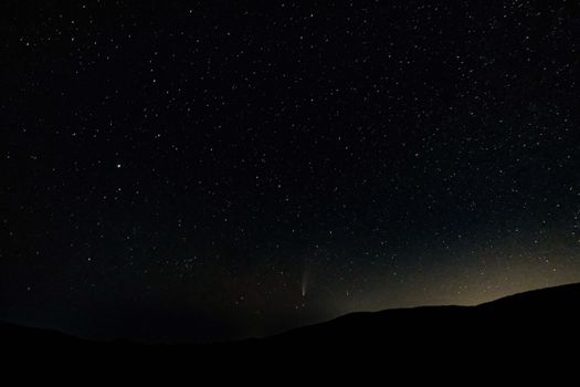在黑暗的山区地形上，壮观的夜空低垂，明亮的星星与坠落的彗星交相辉映
