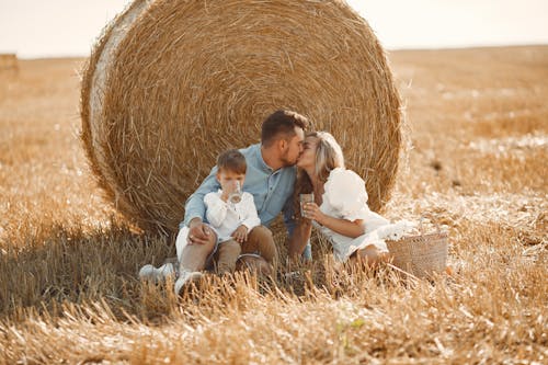 Couple Sitting in Agricultural Field with Son and Kissing