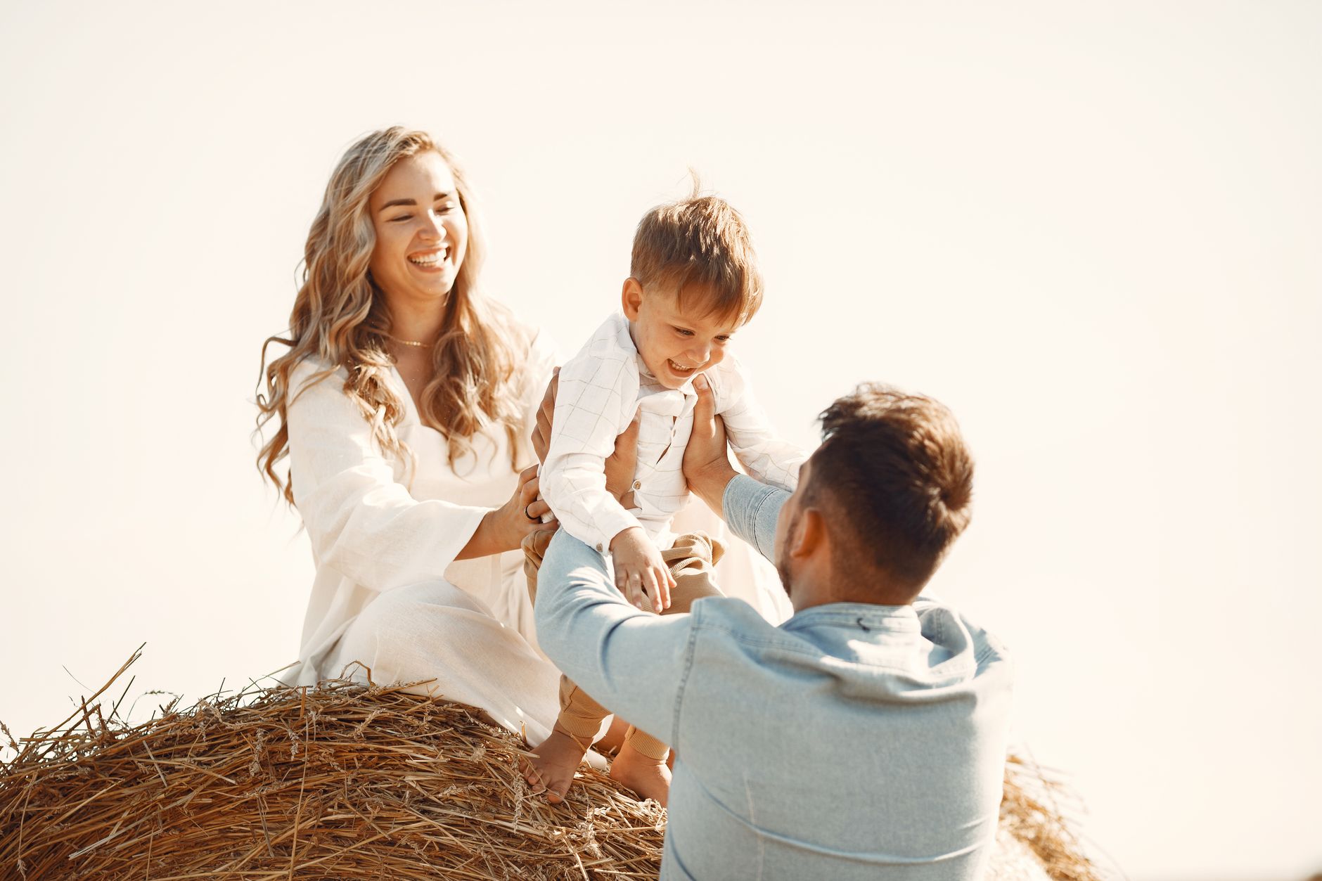 A joyful family enjoying a playful moment on a hay bale under the sun.