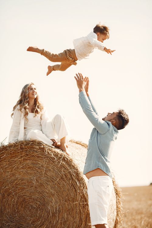 Free Joyful family moment catching son mid-air on hay bale in countryside. Stock Photo