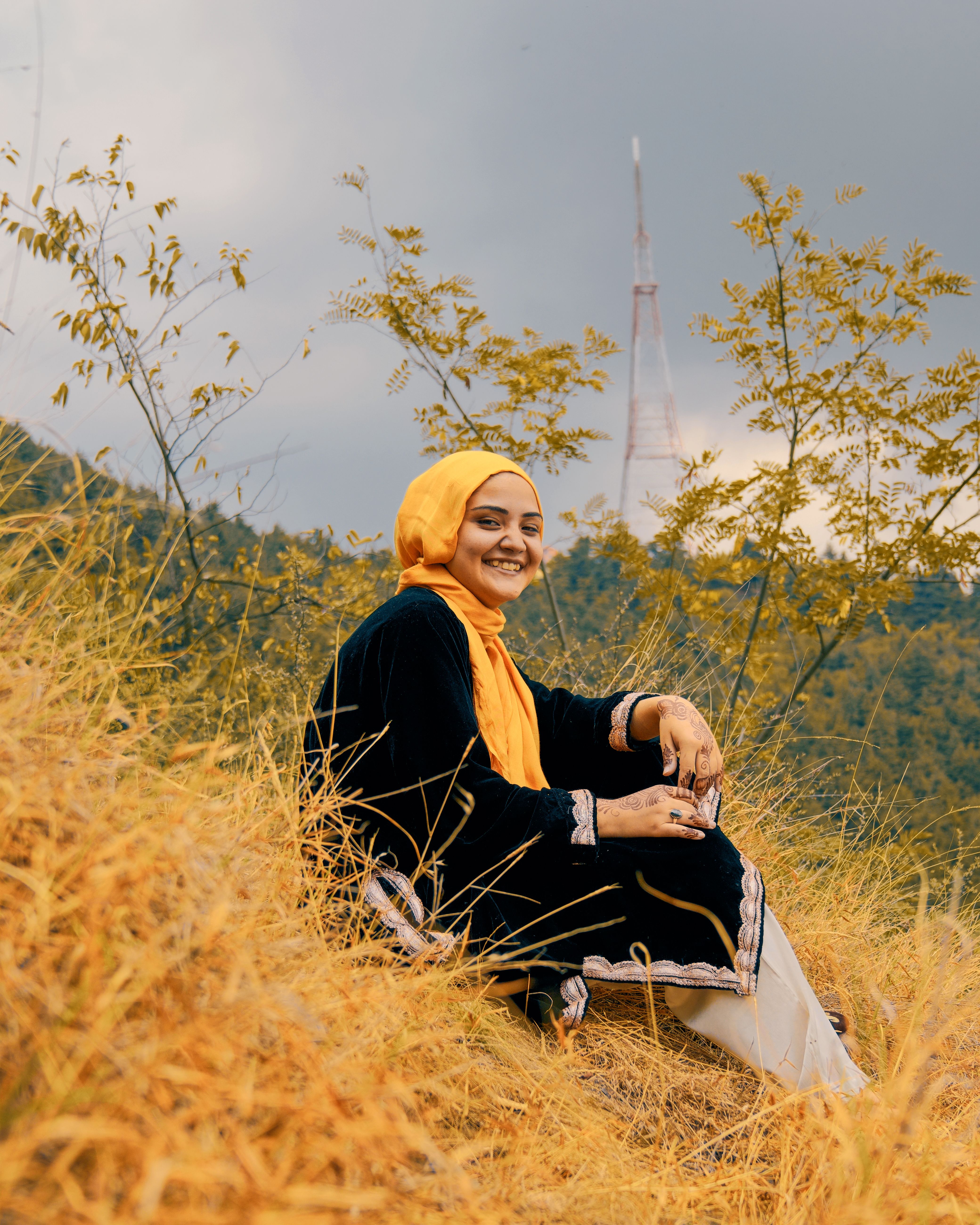 A joyful woman in a hijab sits on a scenic hillside, capturing the essence of nature and tranquility.