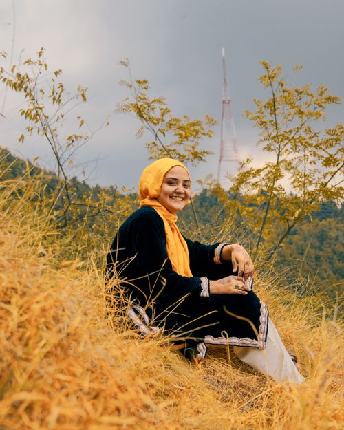 Free A joyful woman in a hijab sits on a scenic hillside, capturing the essence of nature and tranquility. Stock Photo