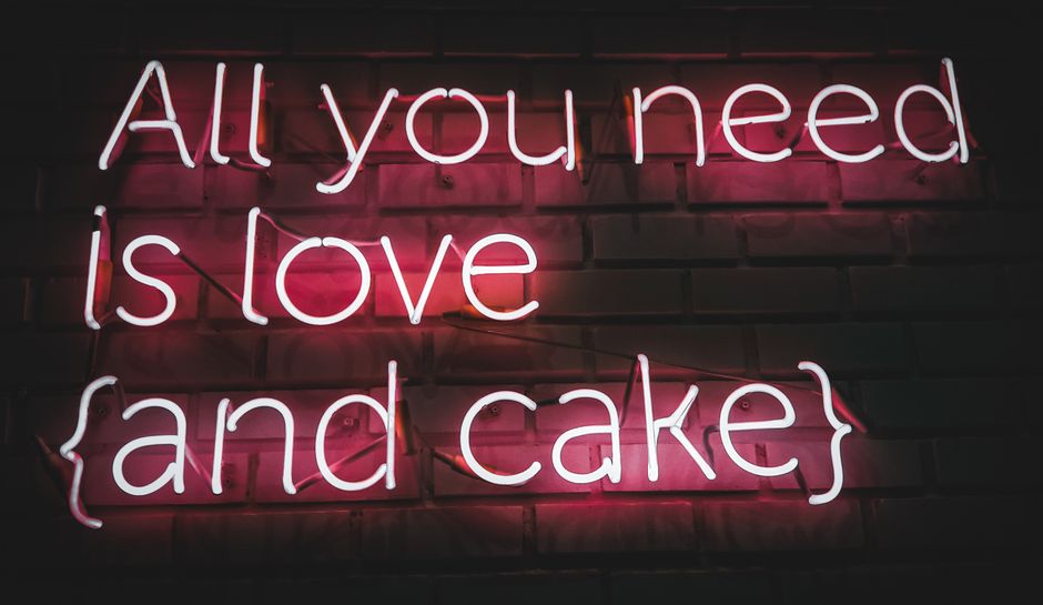 Vibrant pink neon sign with a playful message promoting love and cake.