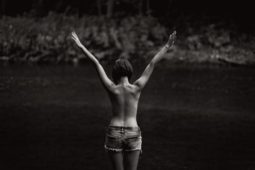 A serene black and white image of a topless woman enjoying nature by a lake.