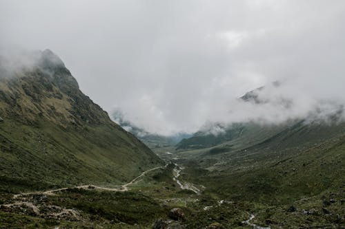 Wide valley surrounded by mountains and branching river under clouds
