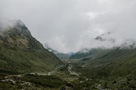 Wide valley surrounded by mountains and branching river under clouds