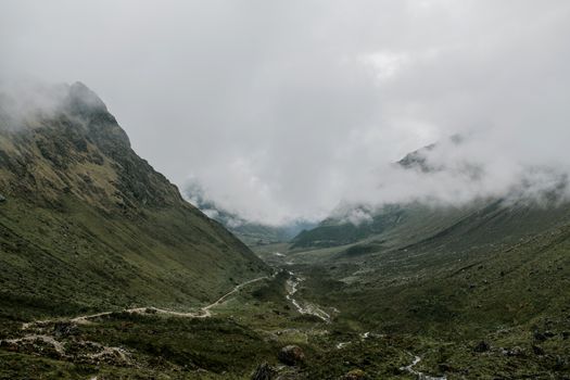 Wide valley surrounded by mountains and branching river under clouds