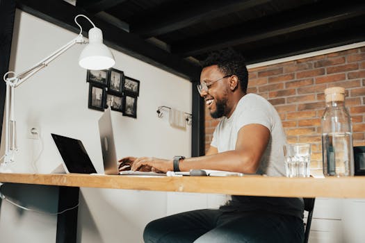 African American man smiling while typing on laptop at home office. Bright and engaging workspace.
