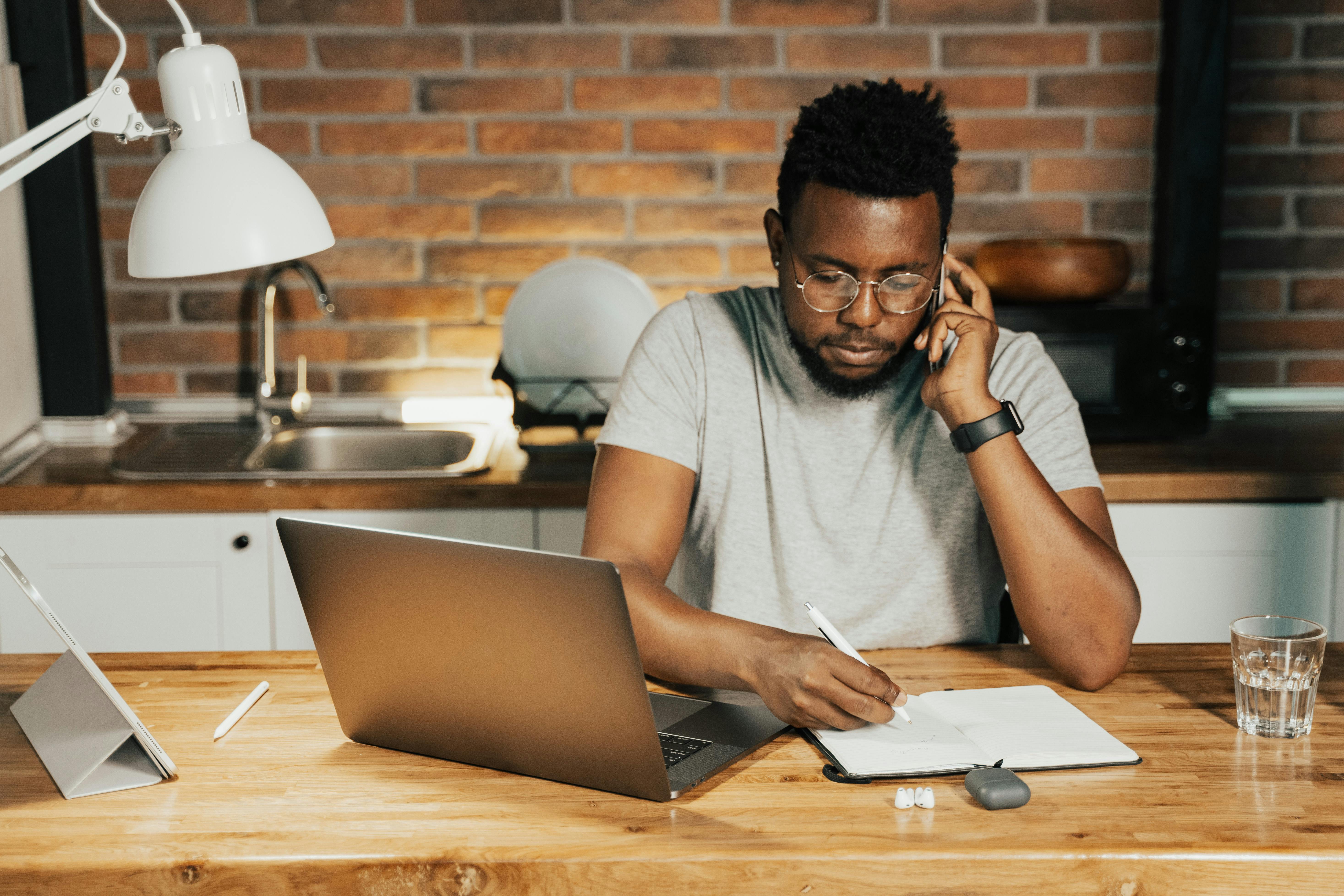 A man working from home with a laptop and notebook, focusing on writing and communication.
