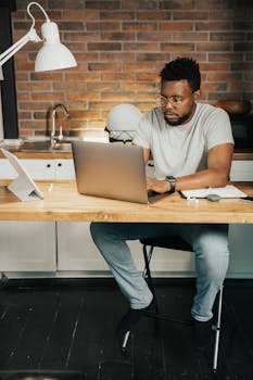 African American man working on a laptop in his home office setting, focusing on remote work tasks.