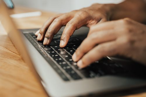 Free Focused shot of hands typing on a laptop keyboard on a wooden table, illustrating remote work. Stock Photo