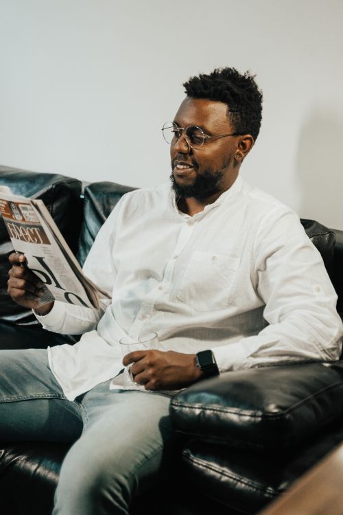 Free A man in a white shirt reading a newspaper while sitting on a leather sofa. Stock Photo