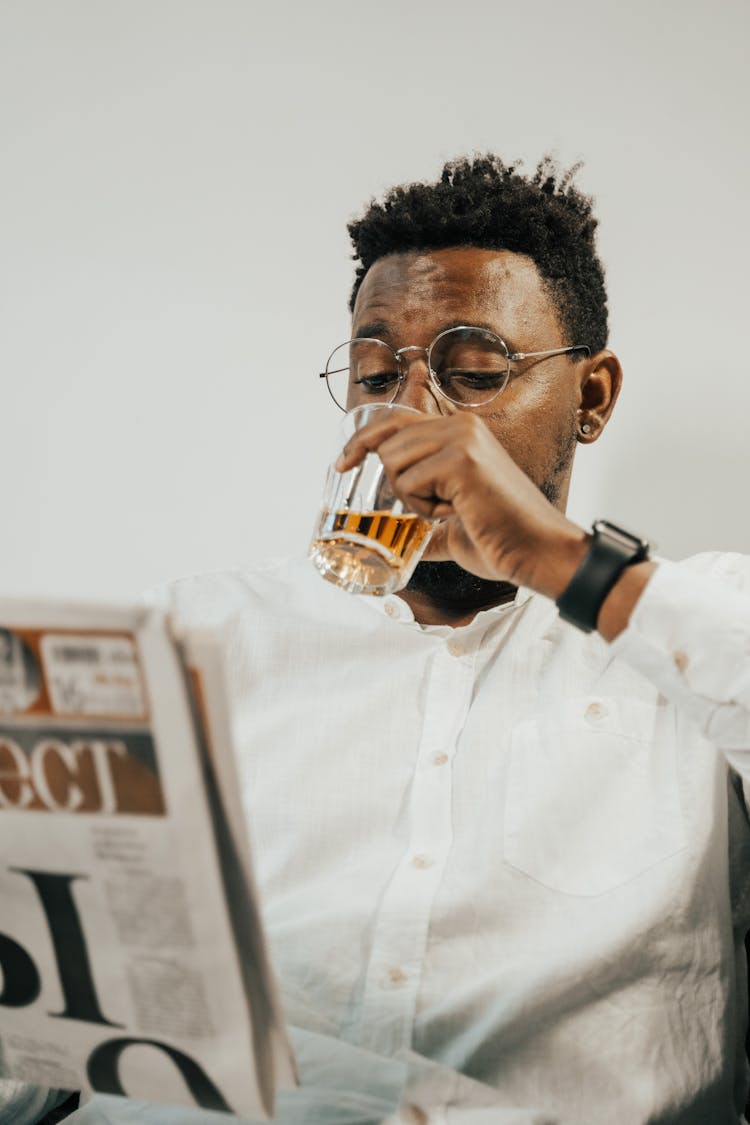 A Man Drinking Beer While Reading Newspaper