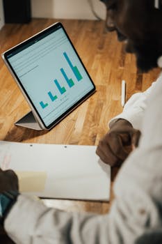 A man working remotely from home using a tablet displaying charts on a wooden table.