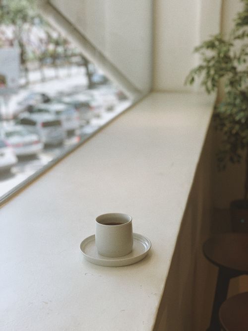 Free Serene indoor scene with a ceramic cup of tea on a windowsill overlooking a blurred city street. Stock Photo