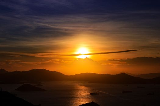 Capturing a vibrant sunset with silhouettes of islands and ships on the ocean horizon.