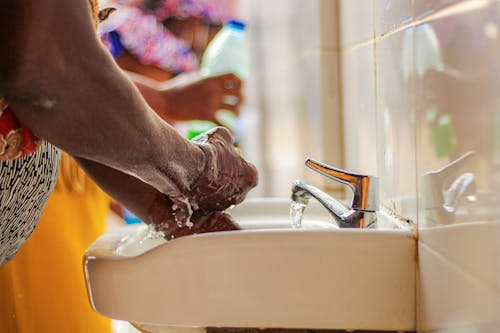 Side view of crop unrecognizable ethnic person in colorful apparel washing hands with soap in sink