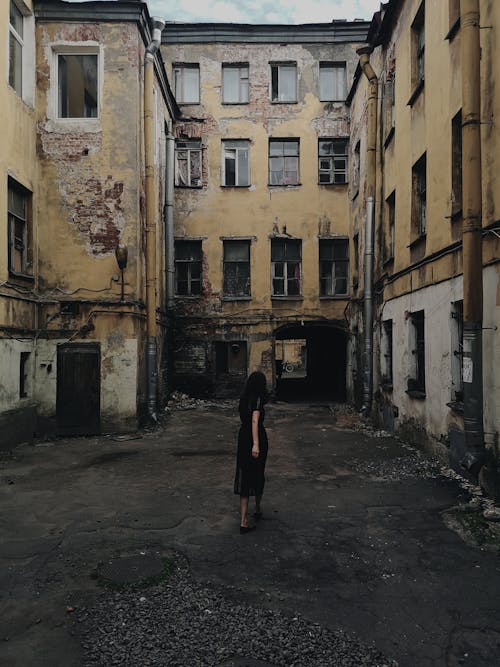 Woman in Black Dress Walking In Front of an Abandoned Building 