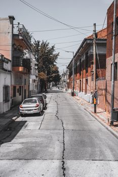 Serene urban street in Buenos Aires, featuring parked cars and red brick buildings under a white sky.